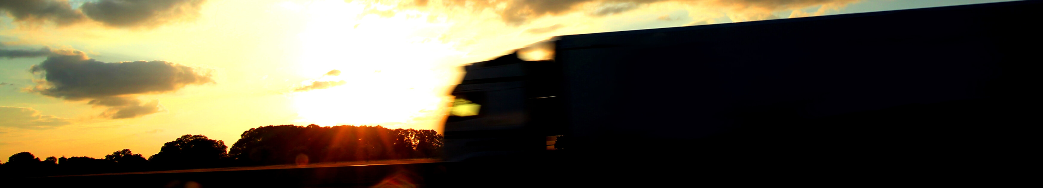 Silhouette eines LKS auf der Autobahn bei Sonnenuntergang und dahinter Bäume
