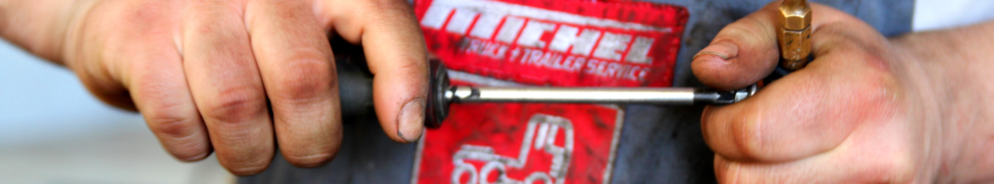 Mitarbeiter einer NKW-Werkstatt mit schmutzigen Händen prüft Schraube mit Schraubendreher